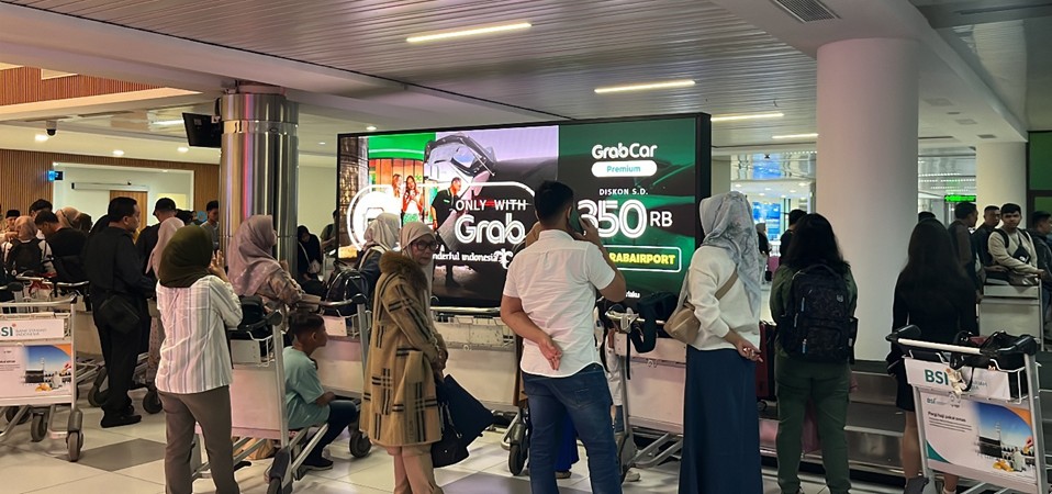 GRAB advertisement on LED screen above baggage conveyor belt at Hang Nadim International Airport in Batam, displayed by The Perfect Media as part creative DOOH campaign