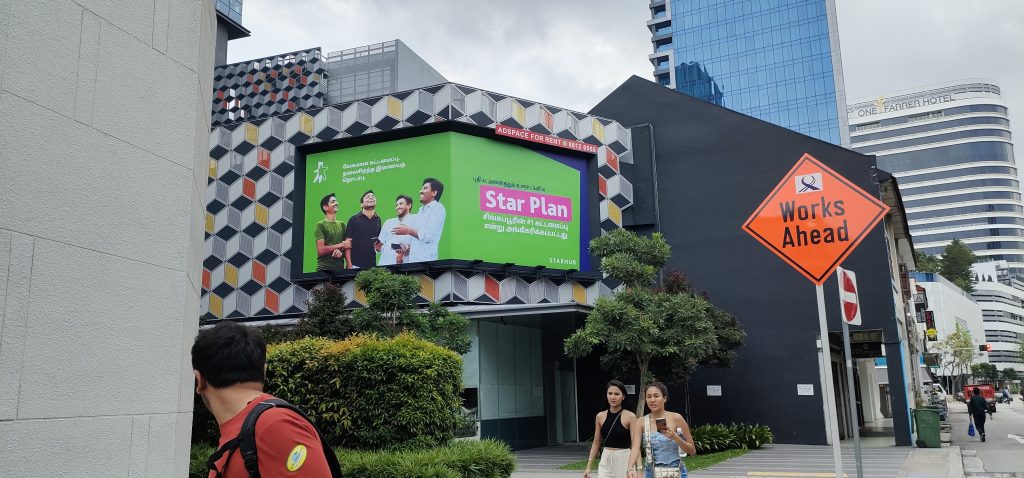 A large LED screen on Kitchener Road, Singapore, displaying the StarHub Star Plan advertisement with a bright green background and a group of young men smiling while holding mobile phones.