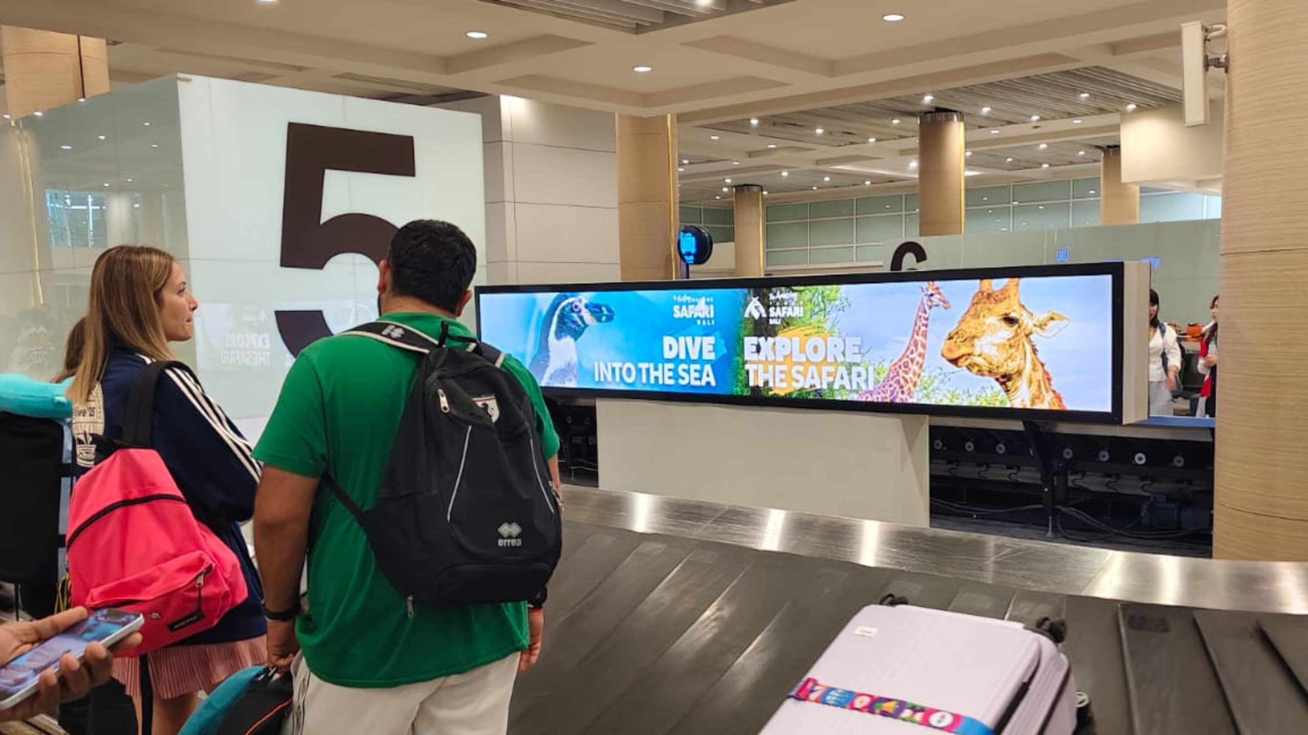 Bali Safari advertising displayed on a long lightbox above the baggage claim conveyor belt, capturing attention of international travelers.