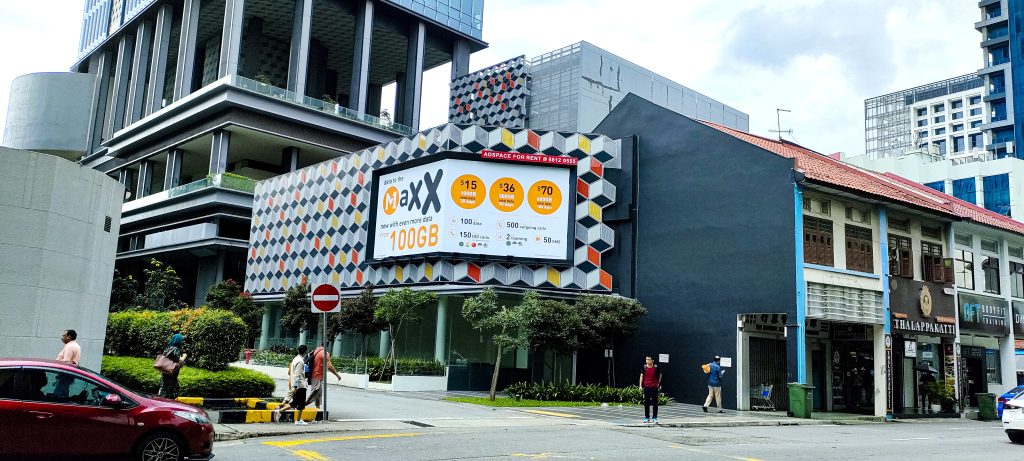 M1 street-level billboard at Centrium Square near Mustafa Centre in Little India, Singapore, highlighting high-visibility outdoor advertising in a busy urban neighborhood